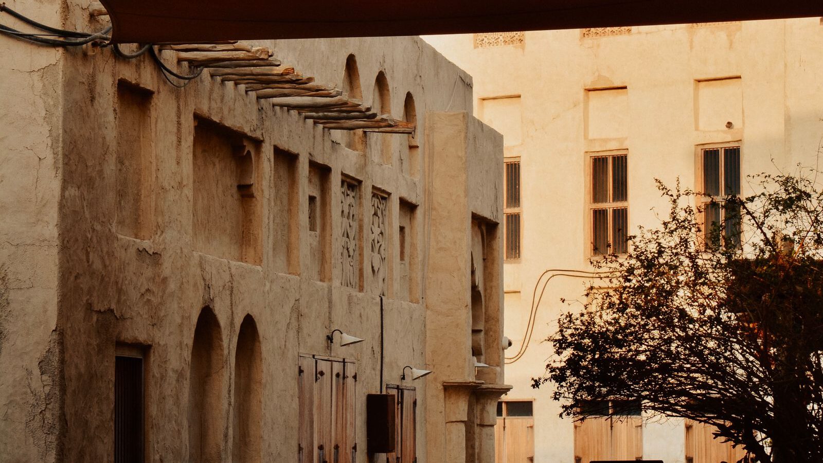 A quiet sand-coloured alley of restored wind-tower merchant houses in Dubai's Al Fahidi Historical Neighbourhood at dusk.