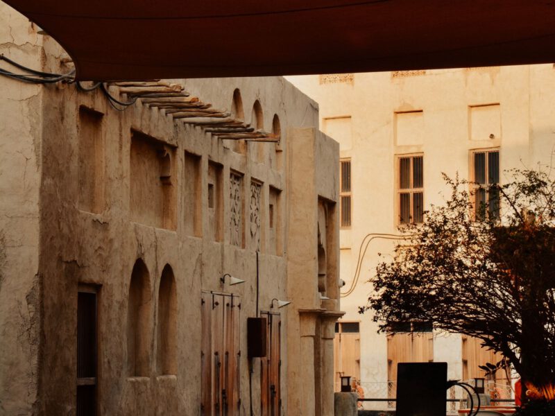 A quiet sand-coloured alley of restored wind-tower merchant houses in Dubai's Al Fahidi Historical Neighbourhood at dusk.