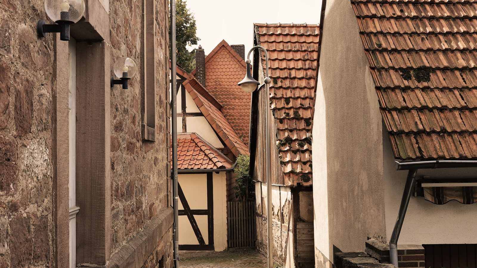 A narrow cobblestone lane between old low houses, evoking the village atmosphere of Böhmisches Dorf Rixdorf in Berlin-Neukölln.