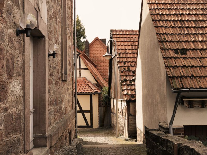 A narrow cobblestone lane between old low houses, evoking the village atmosphere of Böhmisches Dorf Rixdorf in Berlin-Neukölln.