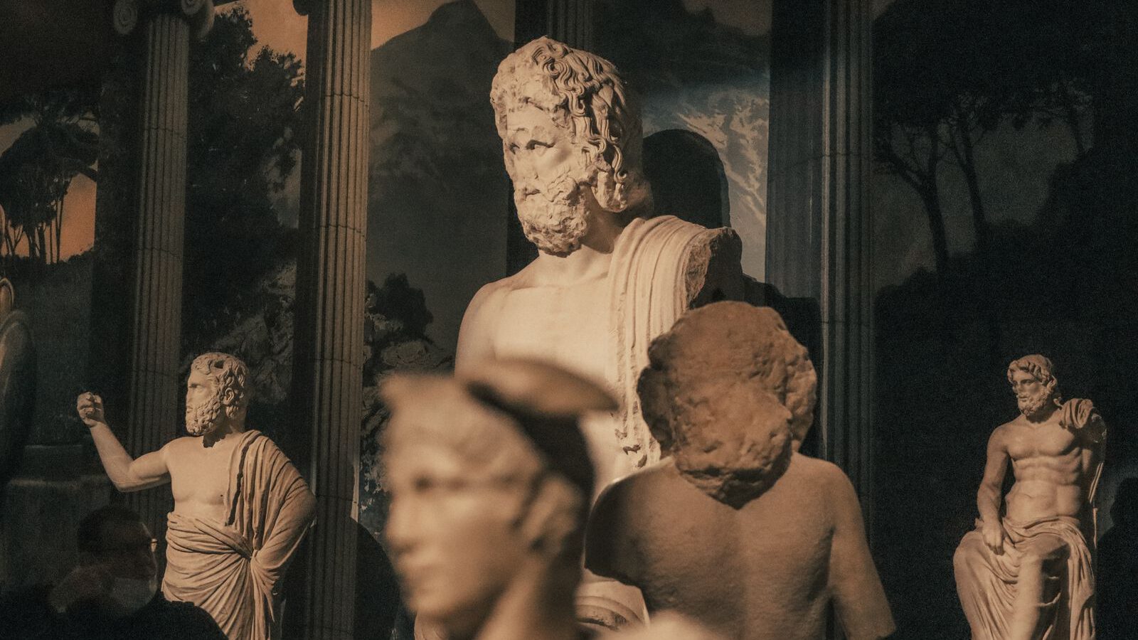 Ancient Roman marble statues of gods and figures dramatically lit against a dark museum backdrop, evoking the classical sculpture at Centrale Montemartini.
