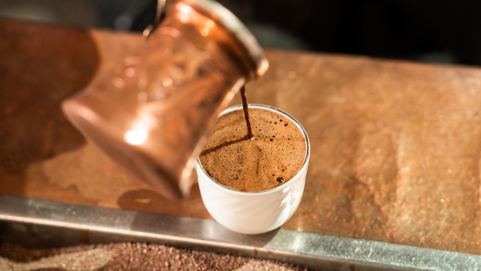 A close-up of freshly brewed coffee being poured from a copper pot into a small white cup, representing the Coffee Museum in Al Fahidi, Dubai.