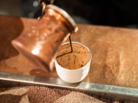 A close-up of freshly brewed coffee being poured from a copper pot into a small white cup, representing the Coffee Museum in Al Fahidi, Dubai.