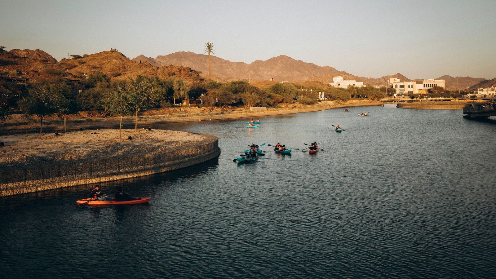 Kayakers paddling across the turquoise Hatta Dam reservoir with the rugged Hajar Mountains behind, in Hatta, Dubai.