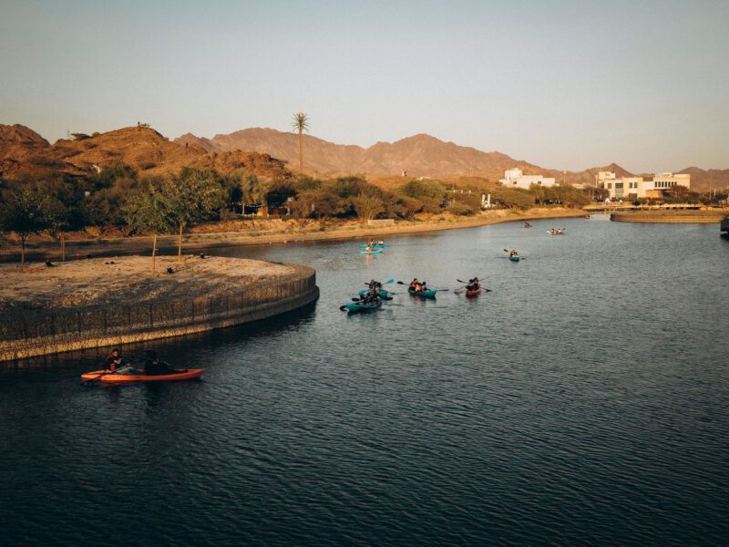 Kayakers paddling across the turquoise Hatta Dam reservoir with the rugged Hajar Mountains behind, in Hatta, Dubai.