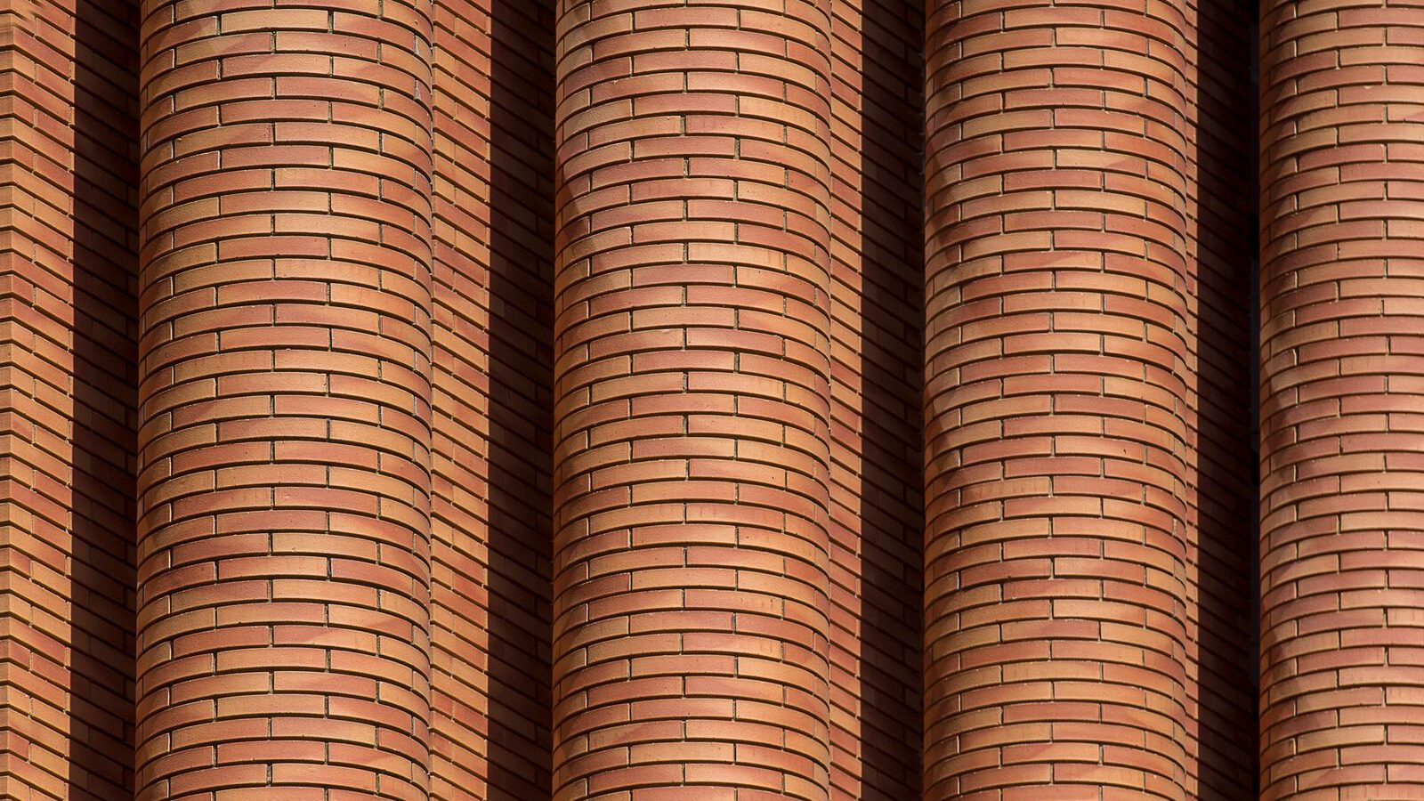 A close-up of curved, sculptural red-brick columns evoking the expressionist brickwork of the Amsterdam School.