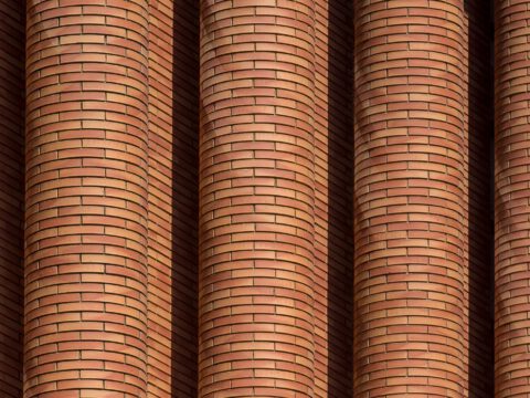 A close-up of curved, sculptural red-brick columns evoking the expressionist brickwork of the Amsterdam School.