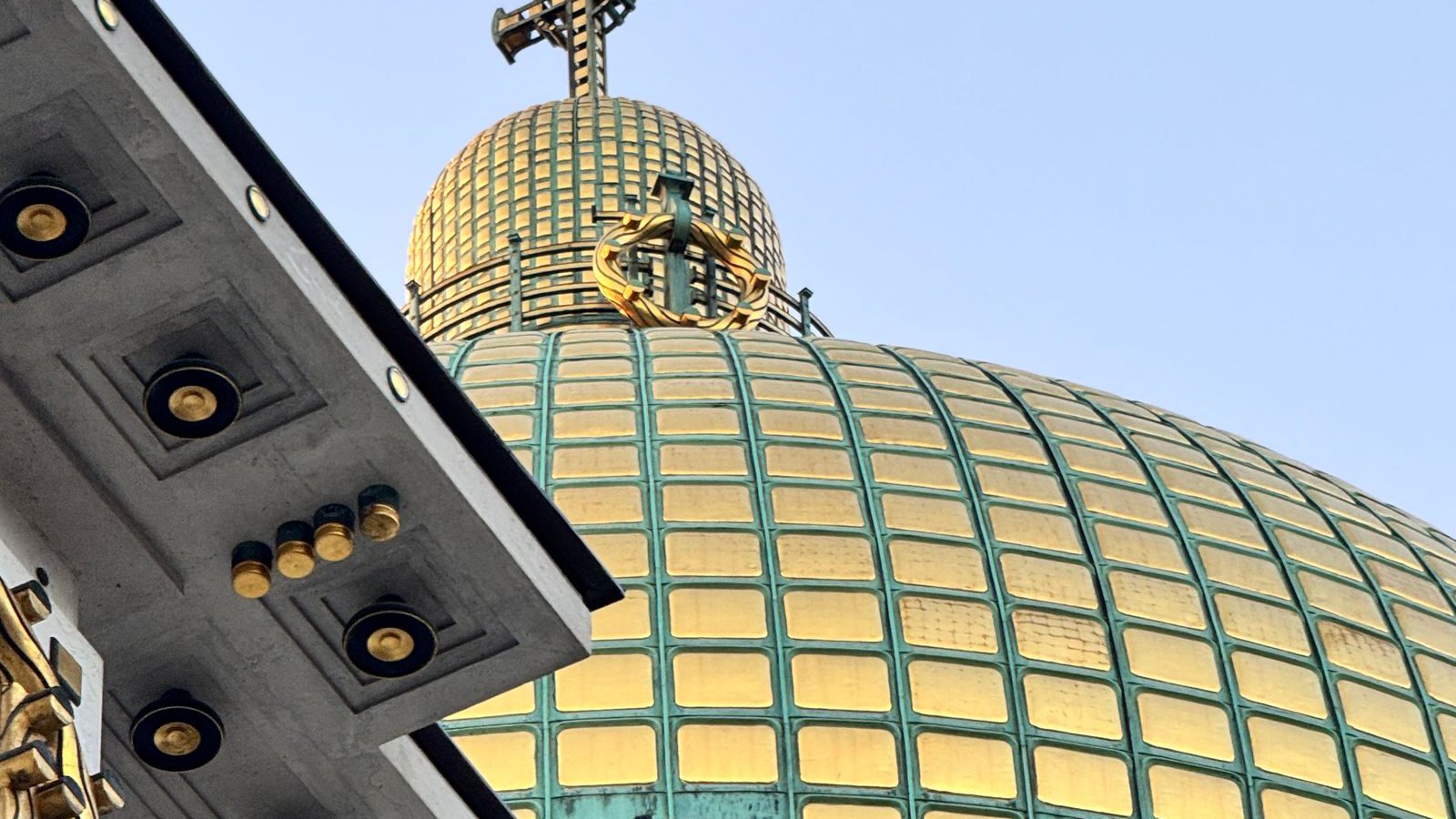 The gilded copper dome and cross of Otto Wagner's Art Nouveau Kirche am Steinhof in Vienna against a clear sky.