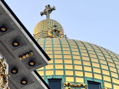 The gilded copper dome and cross of Otto Wagner's Art Nouveau Kirche am Steinhof in Vienna against a clear sky.