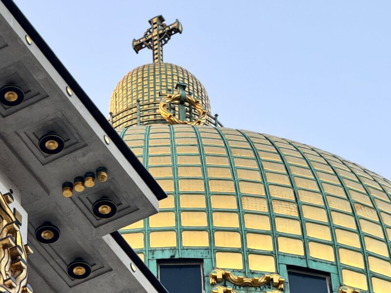 The gilded copper dome and cross of Otto Wagner's Art Nouveau Kirche am Steinhof in Vienna against a clear sky.