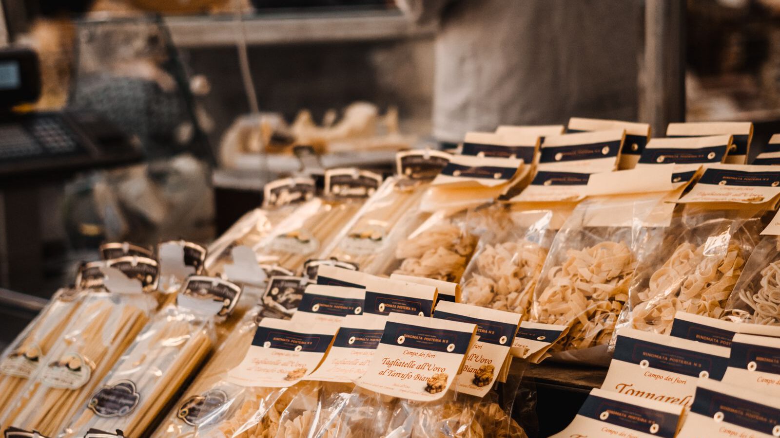 Packages of fresh tonnarelli and artisan pasta piled on an Italian covered-market stall, in the spirit of Rome's Mercato di Testaccio.