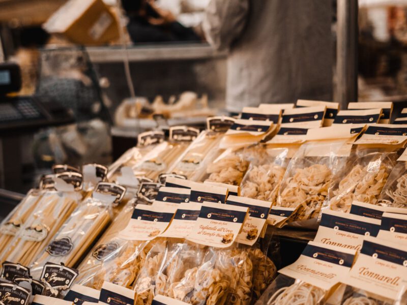 Packages of fresh tonnarelli and artisan pasta piled on an Italian covered-market stall, in the spirit of Rome's Mercato di Testaccio.