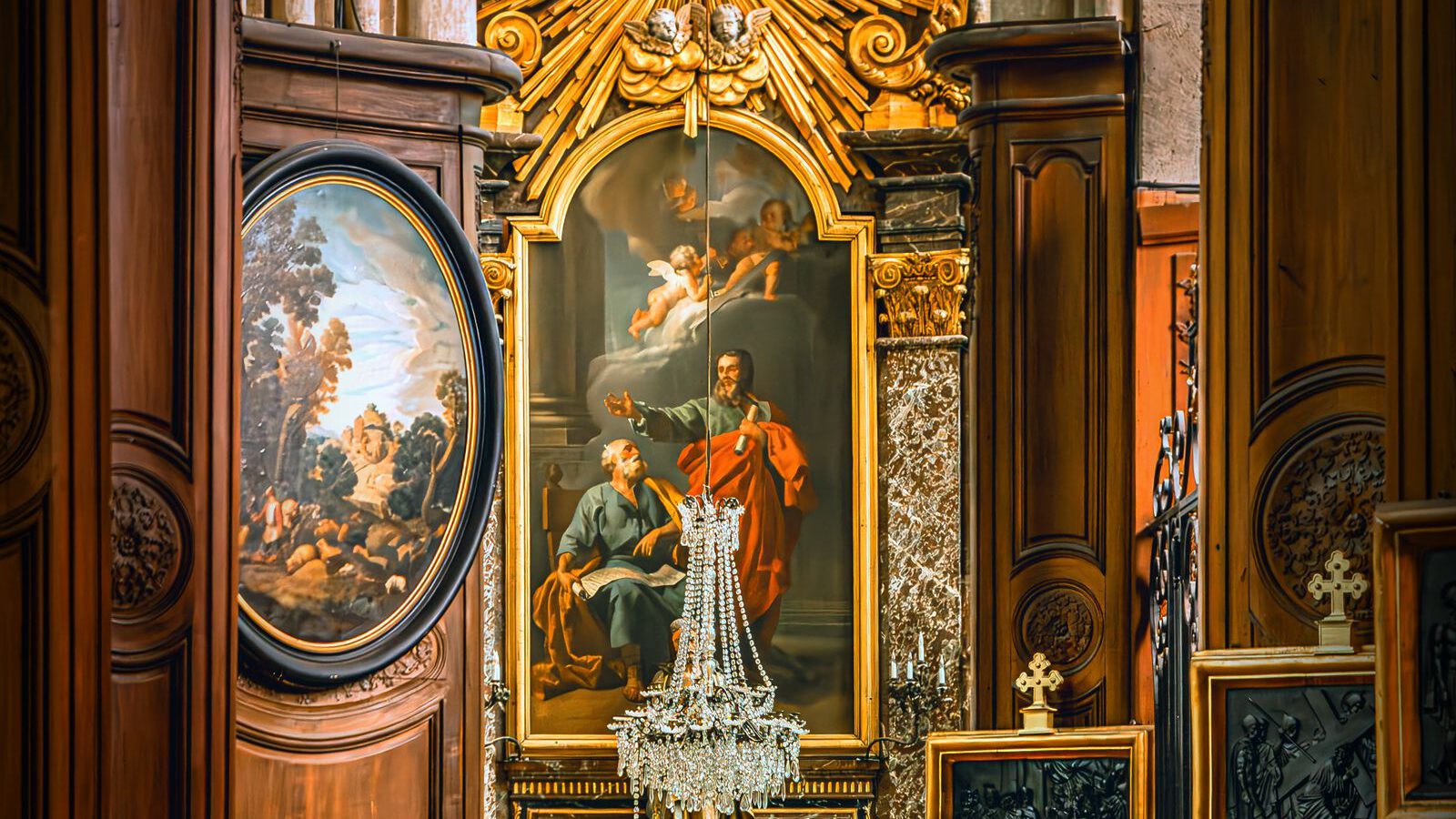 An ornate gilded Baroque altar with a painted altarpiece and a crystal chandelier in a small church interior