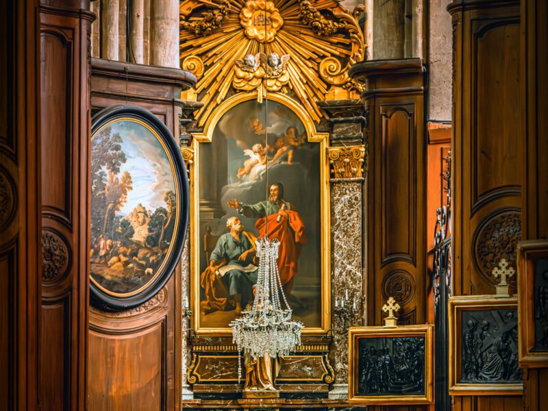 An ornate gilded Baroque altar with a painted altarpiece and a crystal chandelier in a small church interior