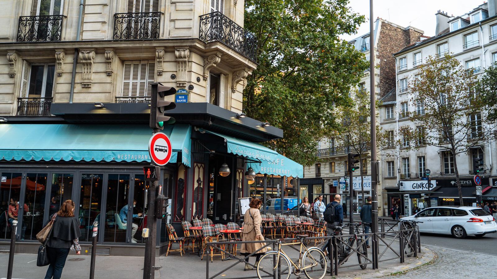 A classic Paris café on a street corner with a turquoise awning, terrace tables and a bicycle, Haussmann buildings behind.