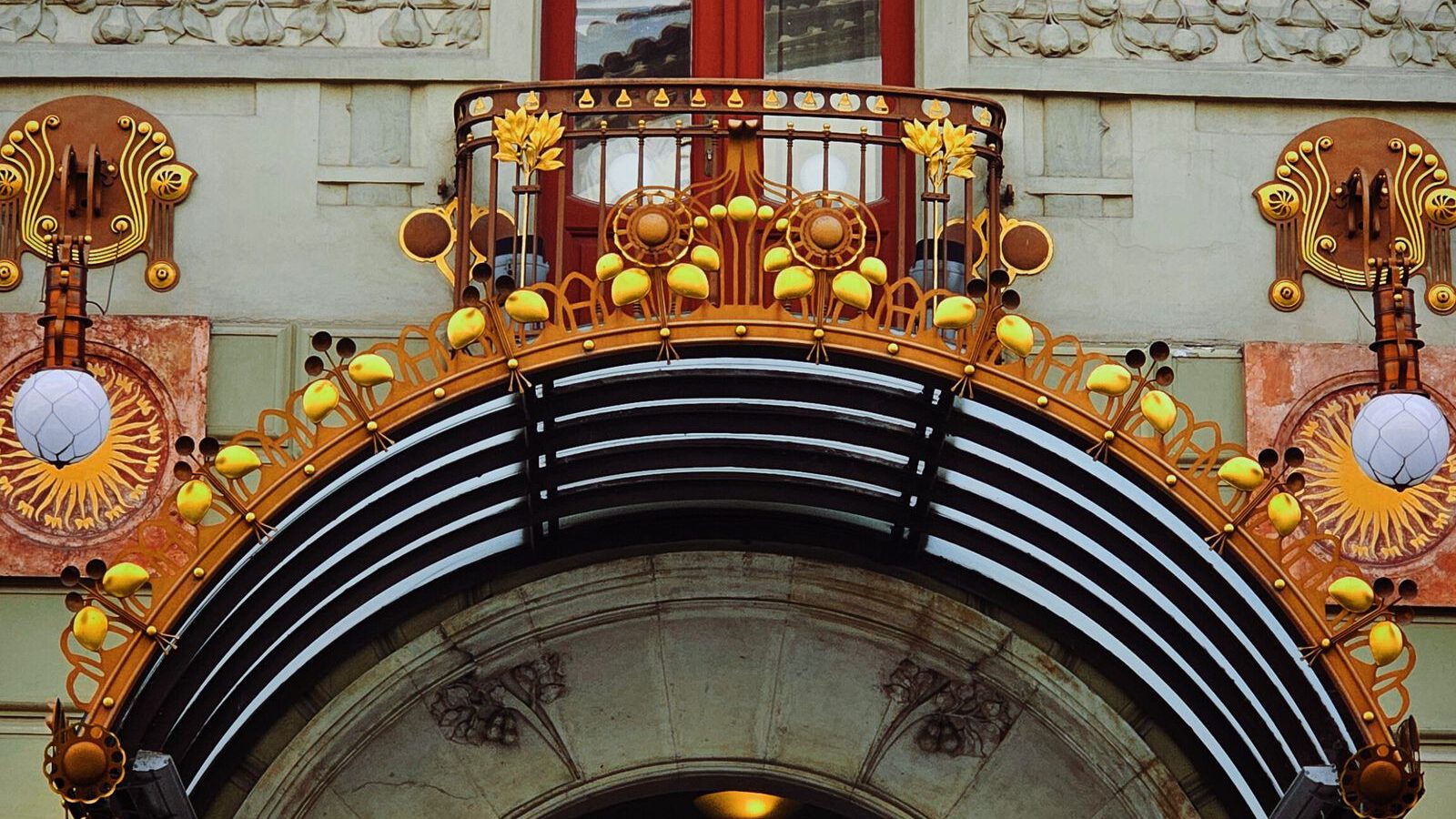 Ornate Art Nouveau facade with a carved face, iron balcony and decorative arch, echoing the fairy-tale architecture of Rome's Quartiere Coppedè.