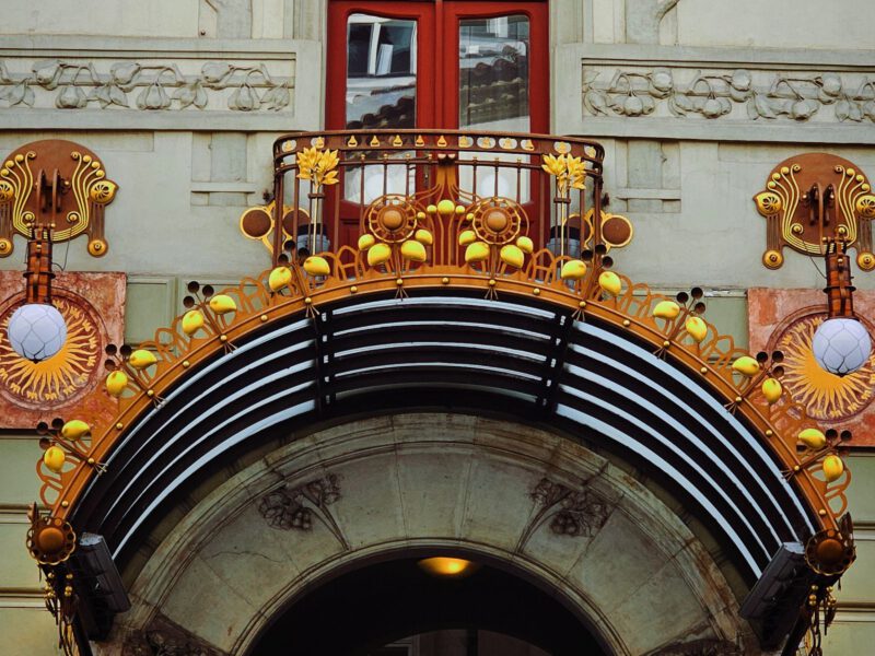 Ornate Art Nouveau facade with a carved face, iron balcony and decorative arch, echoing the fairy-tale architecture of Rome's Quartiere Coppedè.