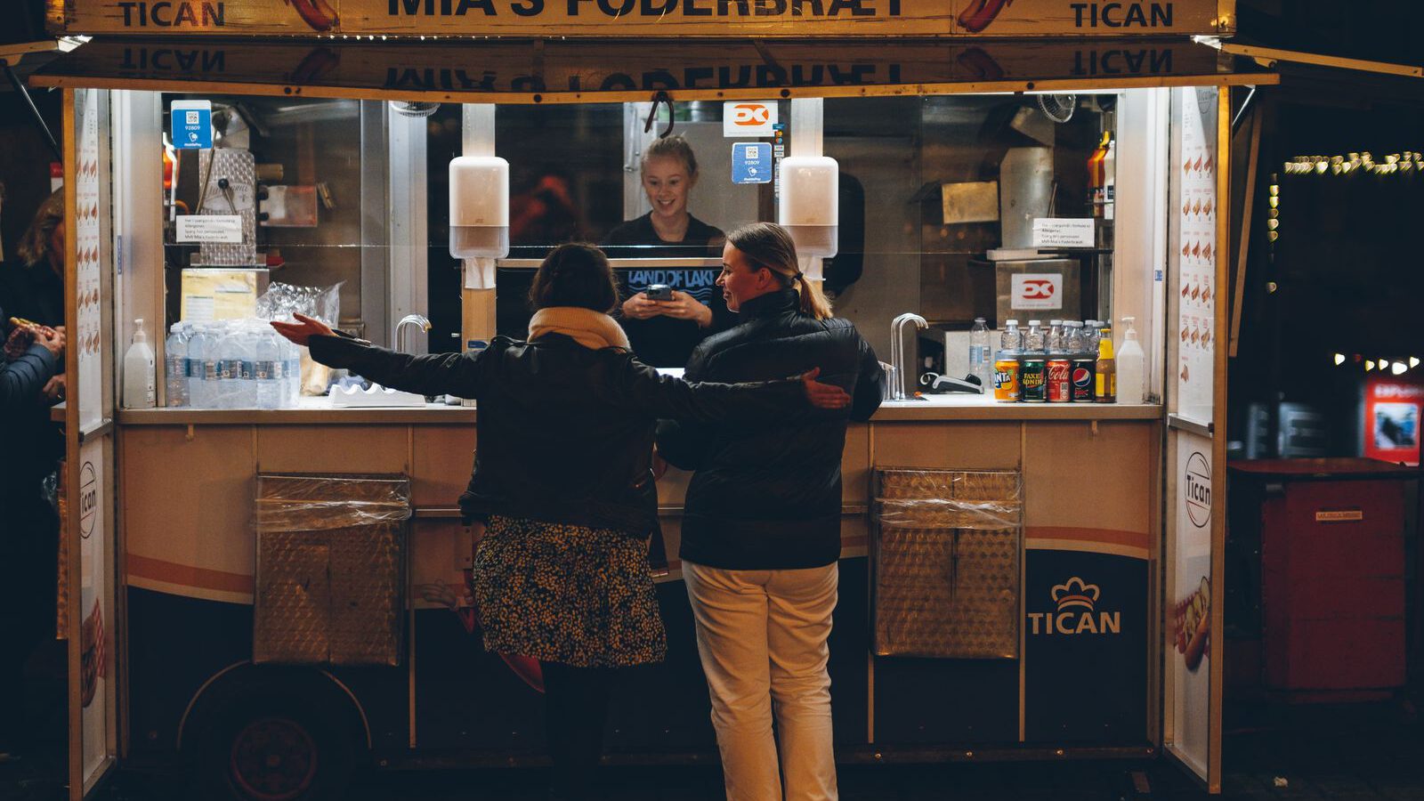Two people ordering from a lit Danish street-food stall at night in Copenhagen.
