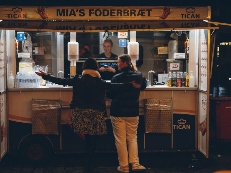 Two people ordering from a lit Danish street-food stall at night in Copenhagen.