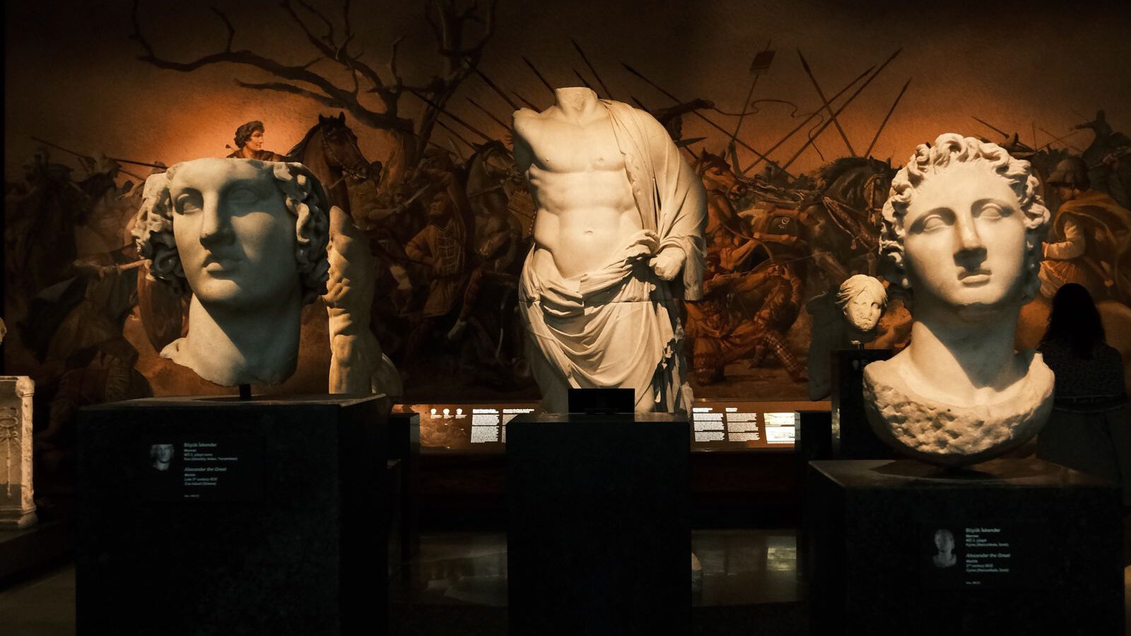 A dimly lit gallery of classical marble statues and busts on plinths