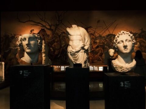 A dimly lit gallery of classical marble statues and busts on plinths