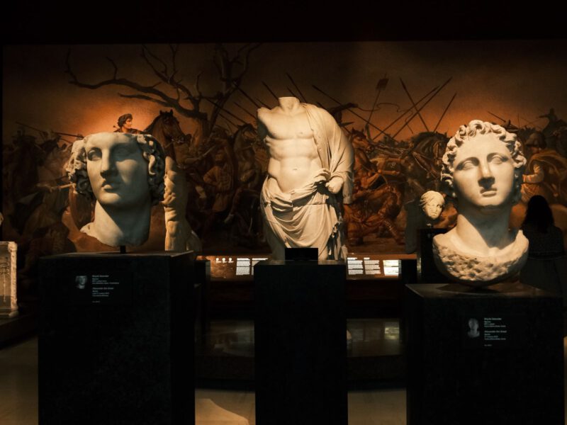 A dimly lit gallery of classical marble statues and busts on plinths