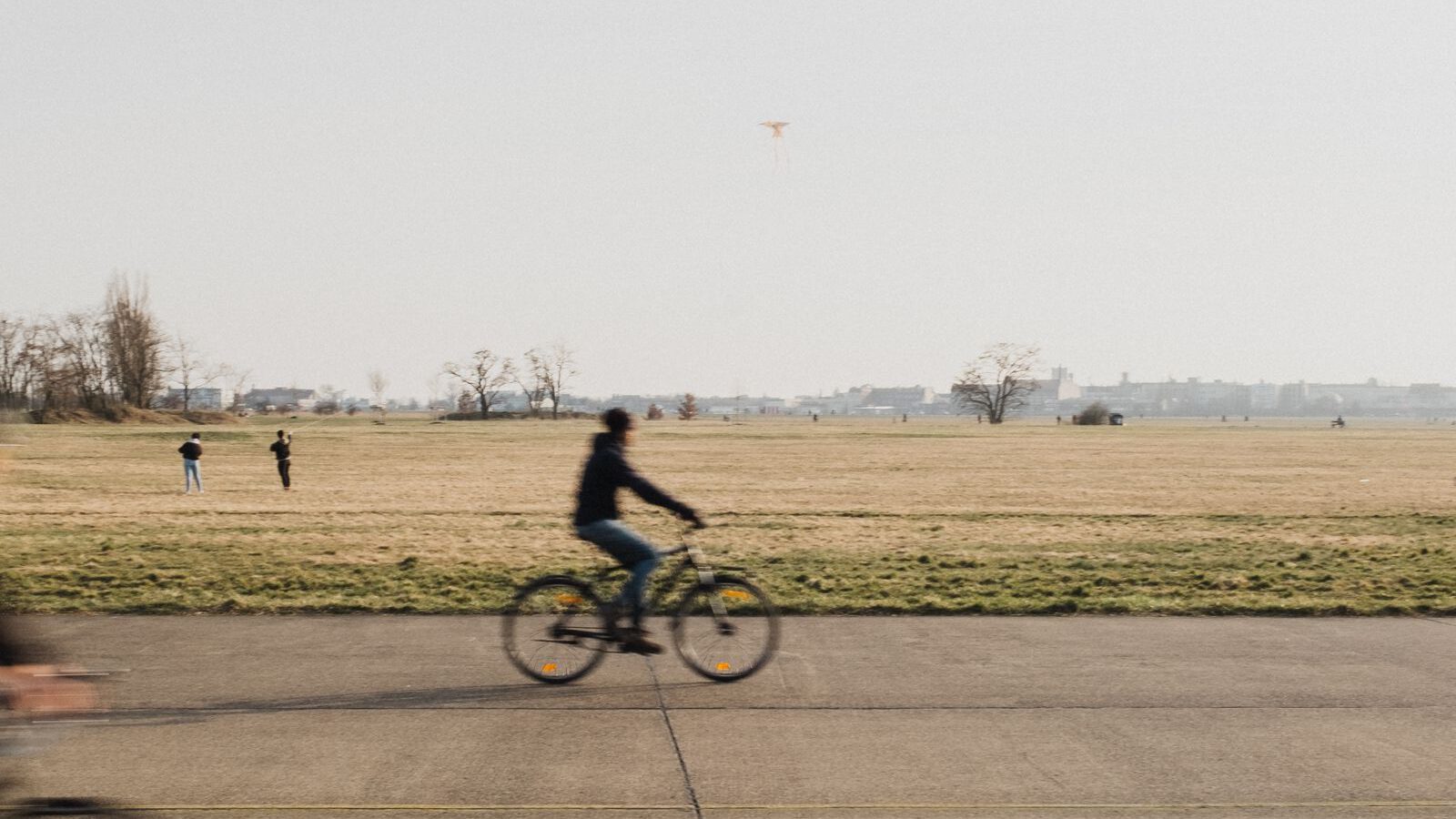 A cyclist crossing the wide former airport runway and open grassland of Tempelhofer Feld in Berlin.