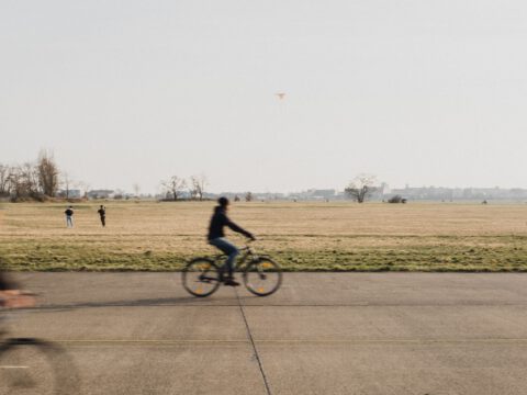 A cyclist crossing the wide former airport runway and open grassland of Tempelhofer Feld in Berlin.